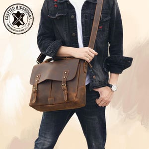 May include: A brown leather messenger bag with a distressed finish. The bag features a flap closure with two buckle straps, a shoulder strap, and the text "CRAFTED HIDEWORKS HANDMADE LEATHER GOODS" in a circular logo.