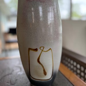 May include: A white ceramic vase with a brown and black design. The vase has a rounded bottom and a narrow opening.