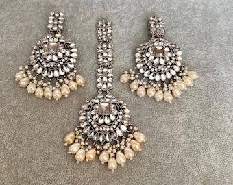 May include: A three-piece jewellery set with a silver finish, comprising a pendant and two earrings. Each piece features a central square stone, surrounded by smaller clear stones and teardrop-shaped faux pearls. Ideal for special events.