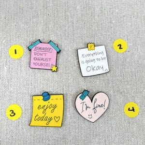 Pode incluir: Quatro pinos de esmalte coloridos com mensagens motivacionais. Os pinos incluem um pino rosa em forma de casa com o texto "REMINDER: DON'T EXHAUST YOURSELF", uma nota branca com "Everything is going to be Okay", uma nota amarela com "enjoy today" e um coração rosa com "I'm fine!"