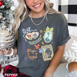 A smiling woman wearing a gray t-shirt with various cartoon characters and designs, including a character with a bow and a character with a snake.