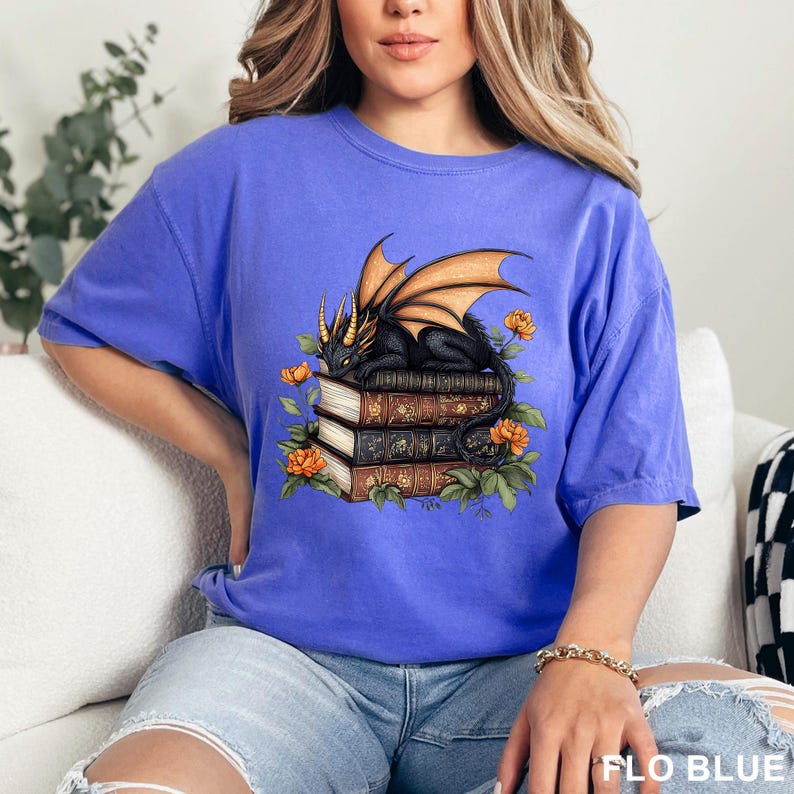 A woman wearing a blue t-shirt with a graphic design of a dragon and books.