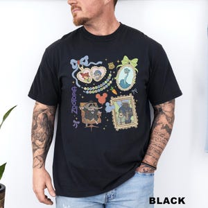 A man wearing a black t-shirt with various cartoon-style illustrations and text, including a character with a bow, a snake, and other whimsical elements.