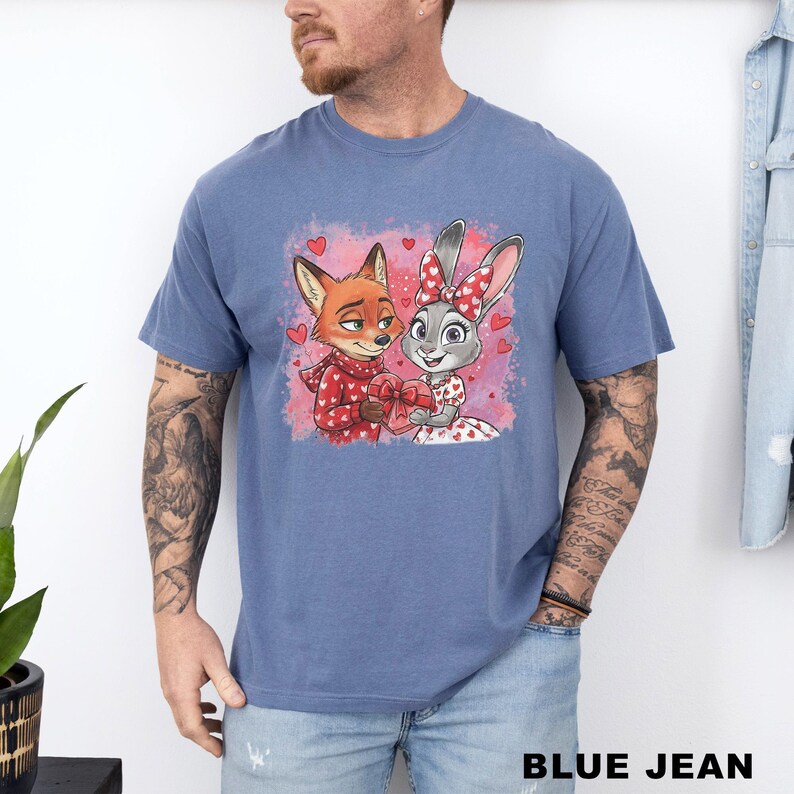 A man wearing a blue t-shirt with a graphic of two cartoon animals, a fox and a rabbit, holding hands and smiling.