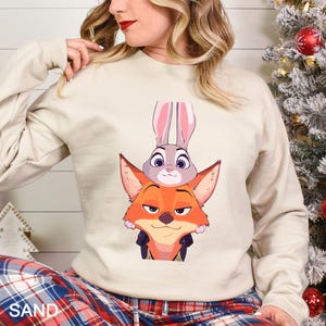 A woman wearing a white sweatshirt with a cartoon image of a fox and a rabbit peeking out from behind it.