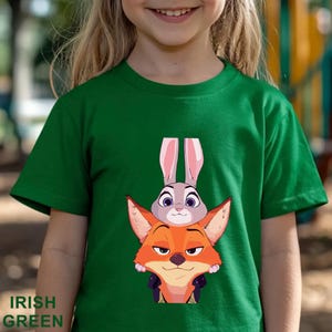 A young girl wearing a green t-shirt with an illustration of a rabbit and a fox on it.