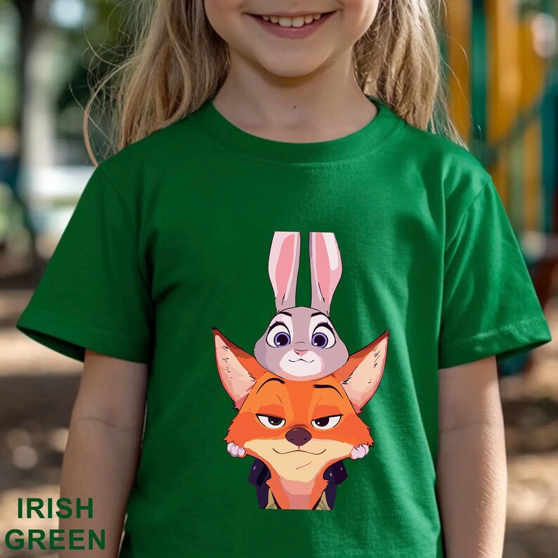 A young girl wearing a green t-shirt with an illustration of a rabbit and a fox on it.