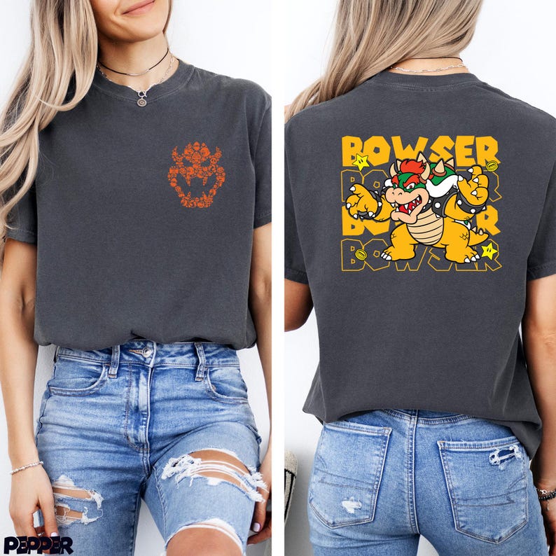 May include: A charcoal gray t-shirt featuring a small orange Bowser shell icon on the front chest. The back displays a large graphic of Bowser with the text BOWSER repeated in yellow, accompanied by small star and coin icons in a vibrant color palette.