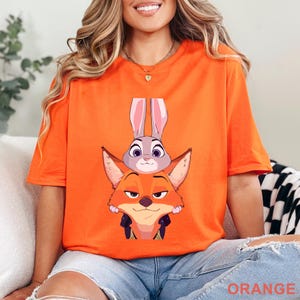 A woman wearing an orange t-shirt with a cartoon rabbit and fox graphic printed on it.
