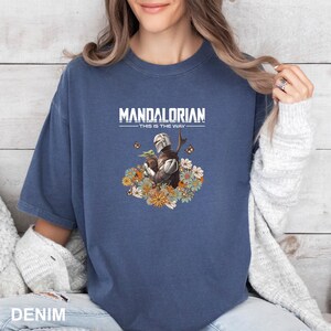 A woman wearing a blue t-shirt with a graphic of a character from the Mandalorian television series.