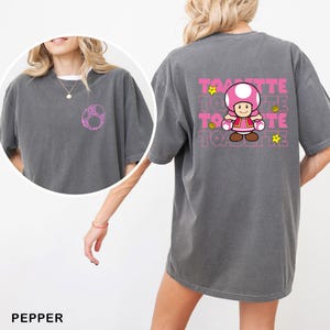 A woman wearing a gray t-shirt with a cartoon character and text printed on the back.