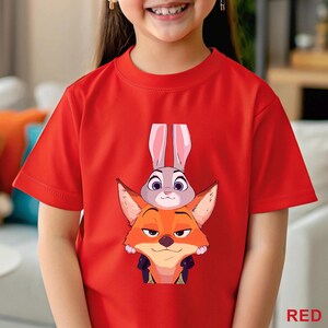 A young girl wearing a red t-shirt with a cartoon image of a fox and a rabbit.