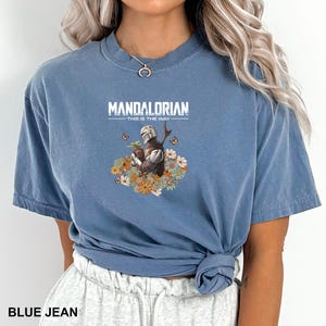 A woman wearing a blue t-shirt with a graphic design of a character from the Mandalorian television series.