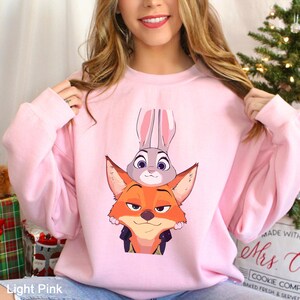 A woman wearing a pink sweatshirt with a cartoon image of a fox and a rabbit on it.