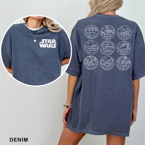 May include: Denim blue t-shirt with the Star Wars logo on the front and nine circular planet designs on the back. The shirt is a relaxed fit and has short sleeves.