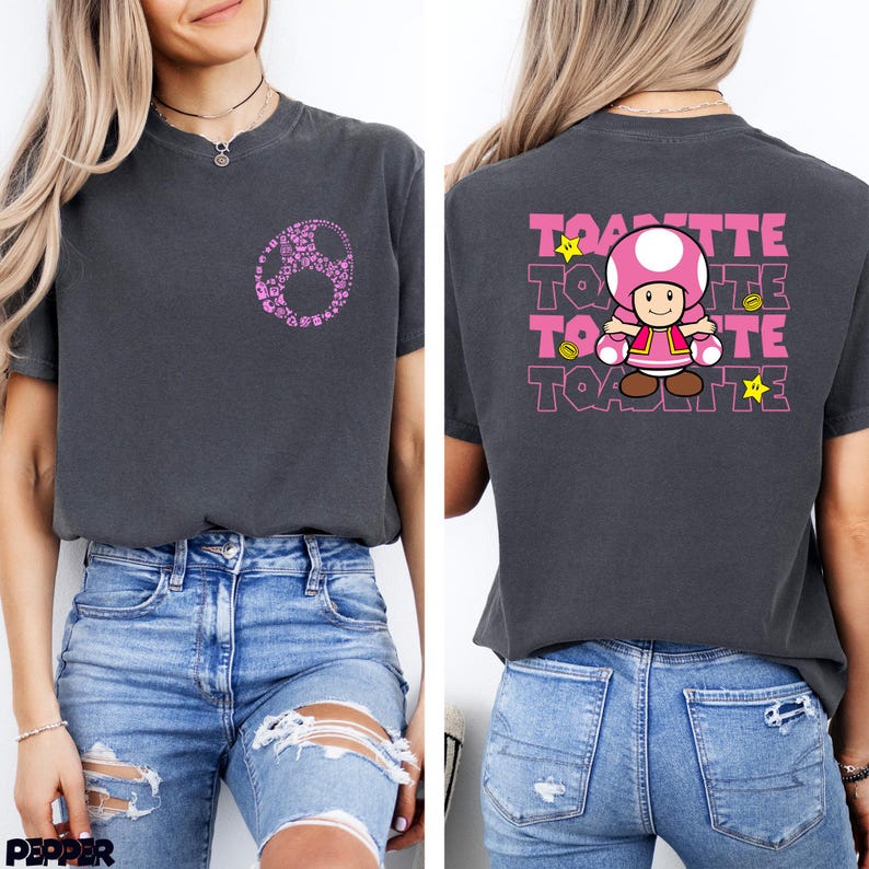 May include: A charcoal gray t-shirt featuring a small pink Toadette mushroom graphic on the front left chest. The back displays a large graphic of the character Toadette with the text TOADETTE repeated in pink and yellow stars and coins.