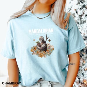 A woman wearing a light blue t-shirt with a graphic of a character from the Mandalorian television series.