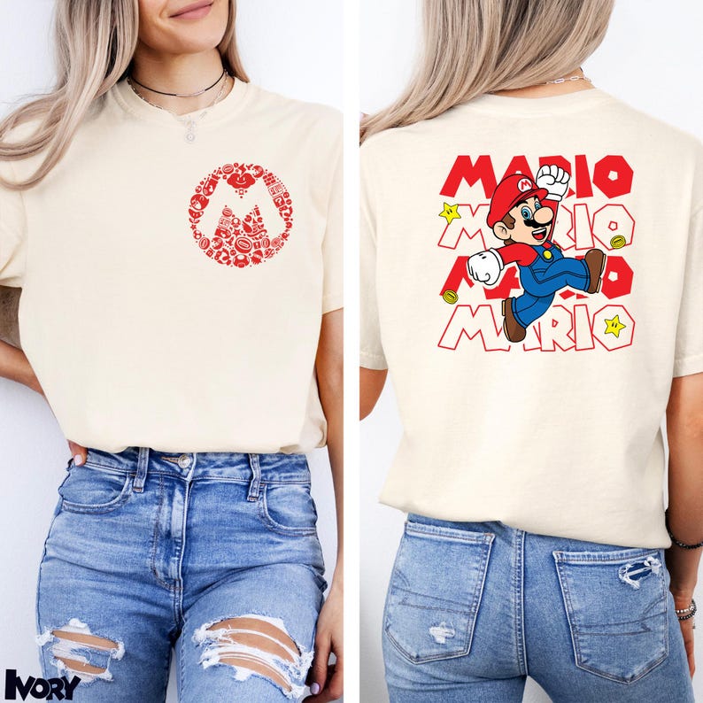 May include: An ivory short-sleeve t-shirt featuring a red circular graphic on the front chest composed of small Mario-themed icons. The back displays a large graphic of Mario jumping with the text MARIO repeated in red block letters and yellow stars.