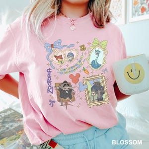 A person wearing a pink t-shirt with various cartoon characters and designs, including a smiling face, holding a coffee mug.