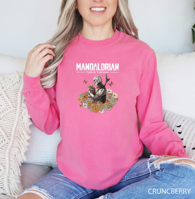 A woman wearing a pink long-sleeved shirt with a graphic design of a character from the Mandalorian television series.