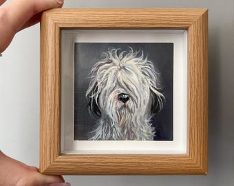 Puede incluir: Pintura enmarcada de un perro lanudo con pelaje blanco y negro. La cara del perro está en su mayor parte oculta por su largo pelaje blanco. La obra de arte está en un marco de madera marrón claro con un passe-partout blanco.