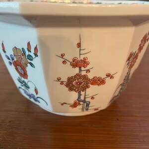 May include: White ceramic planter with a geometric shape and floral design. The planter features red, orange, green, and blue flowers on a white background.