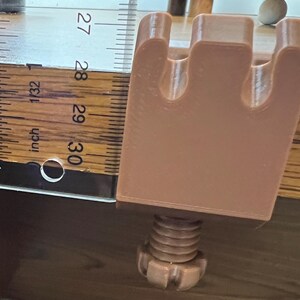 May include: A light brown, 3D-printed C-clamp with a three-pronged top and a threaded screw mechanism at the base. A clear plastic ruler is positioned alongside the clamp, showing the main body height is approximately 1.5 inches tall.