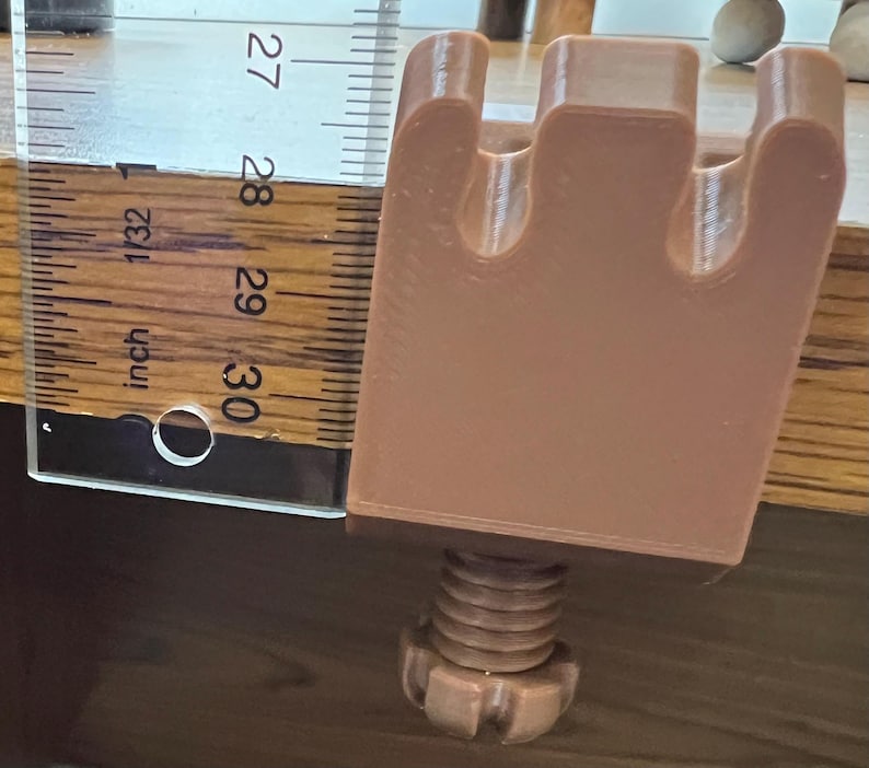 May include: A light brown, 3D-printed C-clamp with a three-pronged top and a threaded screw mechanism at the base. A clear plastic ruler is positioned alongside the clamp, showing the main body height is approximately 1.5 inches tall.