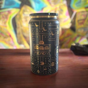 May include: Black and gold stainless steel water bottle with a Pac-Man themed design. The bottle features a Pac-Man maze with ghosts, cherries, and the text "READY!"