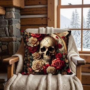 Könnte beinhalten: Ein dekoratives Kissen mit einem Totenkopf-Design, umgeben von roten und cremefarbenen Rosen. Der Schädel hat ein rissiges Aussehen, und das Kissen liegt auf einem Holzstuhl mit einem Strickwurf. Der Hintergrund zeigt ein Fenster mit einer verschneiten Landschaft.