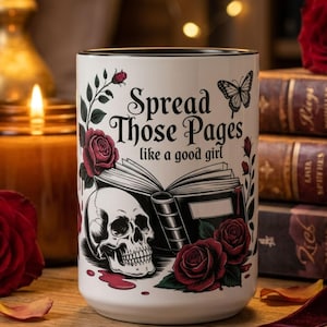 May include: White ceramic mug with black rim featuring the text "Spread Those Pages like a good girl". The mug has a skull, roses, and a butterfly design. The background includes a candle, roses, and books.