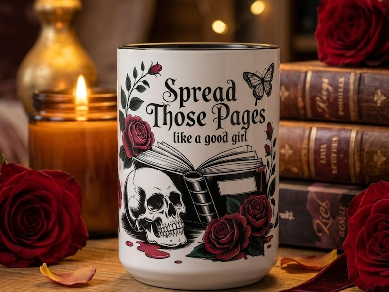 May include: White ceramic mug with black rim featuring the text "Spread Those Pages like a good girl". The mug has a skull, roses, and a butterfly design. The background includes a candle, roses, and books.