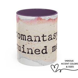May include: A ceramic mug with a purple interior and a speckled, off-white exterior. The mug features the text "romantasy ruined me" in a black, typewriter-style font. The design includes watercolor-style pink and white accents.