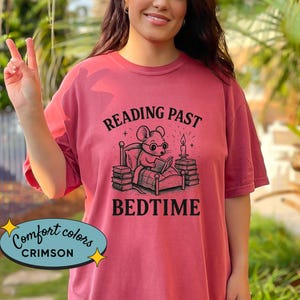 Peut inclure: T-shirt Comfort Colors couleur cramoisi avec le texte "READING PAST BEDTIME" et un dessin d'une souris lisant au lit. Le t-shirt est de couleur cramoisi uni.