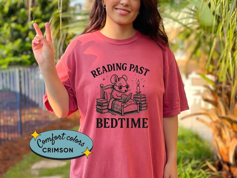 Peut inclure: T-shirt Comfort Colors couleur cramoisi avec le texte "READING PAST BEDTIME" et un dessin d'une souris lisant au lit. Le t-shirt est de couleur cramoisi uni.