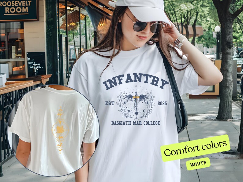 Puede incluir: Camiseta blanca con un estampado gr&aacute;fico azul de un drag&oacute;n con alas y el texto "INFANTRY EST 2025 BASSGIATH WAR COLLEGE". El texto "Comfort colors WHITE" es visible en la esquina inferior derecha de la imagen.