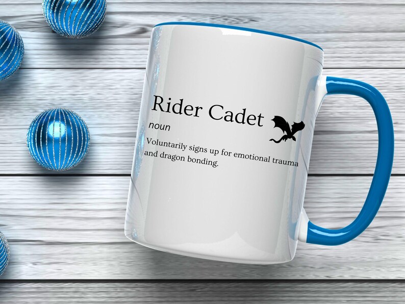 May include: White ceramic mug with a blue handle and rim, featuring the text "Rider Cadet" and a dragon silhouette. The mug's definition humorously describes the role. Decorative blue spheres are in the background.