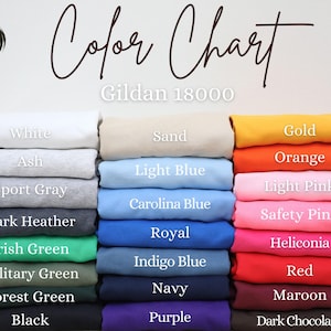 以下が含まれることがあります： さまざまな色のGildan 18000のスウェットシャツが折りたたまれたカラーチャート。白、アッシュ、スポーツグレー、ダークヘザー、黒など。チャートには「Color Chart」の文字も含まれています。