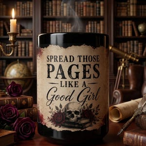 Op de afbeelding: Een zwarte keramische mok met een beige perkamentachtige afbeelding met de tekst "SPREAD THOSE PAGES LIKE A GOOD GIRL" in zwarte letters, vergezeld van een illustratie van een menselijke schedel op boeken omringd door donkerrode rozen.