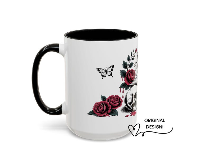 May include: White ceramic mug with a black handle and interior. The mug features a design of a skull, roses, and a butterfly. The words "ORIGINAL DESIGN!" are written on the mug.