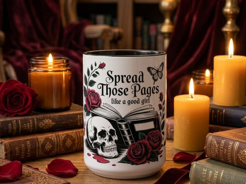 May include: A white ceramic mug with a black interior, featuring a skull, roses, and the text "Spread Those Pages like a good girl." The mug is surrounded by lit candles, books, and red rose petals.