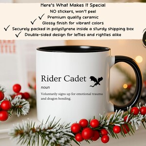 May include: White ceramic mug with a black interior and handle. The mug features the text "Rider Cadet" with a dragon graphic. The mug is decorated with holiday greenery and red berries. The mug is double-sided.