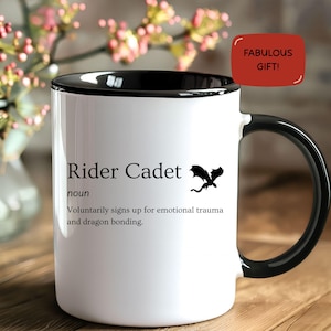May include: White ceramic mug with a black handle and rim. The mug features the text "Rider Cadet" with a dragon graphic and the phrase "Voluntarily signs up for emotional trauma and dragon bonding." A red tag reads "FABULOUS GIFT!"
