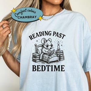 Peut inclure: T-shirt bleu clair avec une illustration en noir et blanc d'une souris lisant au lit, avec les mots "READING PAST BEDTIME". Le t-shirt porte &eacute;galement les mots "Comfort Colors CHAMBRAY" dans un ovale bleu clair.