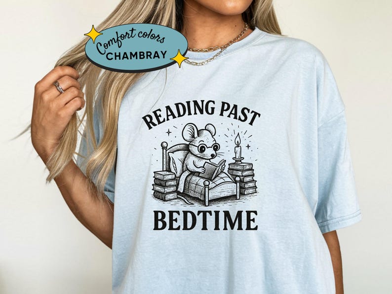 Peut inclure: T-shirt bleu clair avec une illustration en noir et blanc d'une souris lisant au lit, avec les mots "READING PAST BEDTIME". Le t-shirt porte &eacute;galement les mots "Comfort Colors CHAMBRAY" dans un ovale bleu clair.