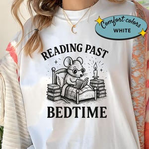 Peut inclure: T-shirt blanc avec un dessin en noir et blanc d'une souris lisant au lit, avec le texte "READING PAST BEDTIME". Le t-shirt porte &eacute;galement une &eacute;tiquette Comfort Colors.