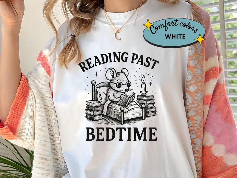 Peut inclure: T-shirt blanc avec un dessin en noir et blanc d'une souris lisant au lit, avec le texte "READING PAST BEDTIME". Le t-shirt porte &eacute;galement une &eacute;tiquette Comfort Colors.