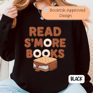 以下が含まれることがあります： 茶色の文字で「READ S'MORE BOOKS」と書かれた黒いスウェットシャツ。スモアのグラフィック付き。「Booktok-Approved」のデザイン。「BLACK」の文字は白い長方形の中にある。
