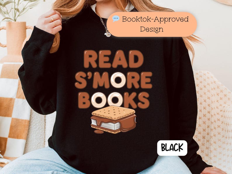 以下が含まれることがあります： 茶色の文字で「READ S'MORE BOOKS」と書かれた黒いスウェットシャツ。スモアのグラフィック付き。「Booktok-Approved」のデザイン。「BLACK」の文字は白い長方形の中にある。