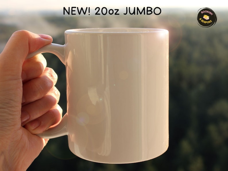 May include: A jumbo-sized, off-white ceramic mug with a curved handle. The mug is labeled "NEW! 20oz JUMBO" in black text. The mug is held by a hand, with a blurred green background.